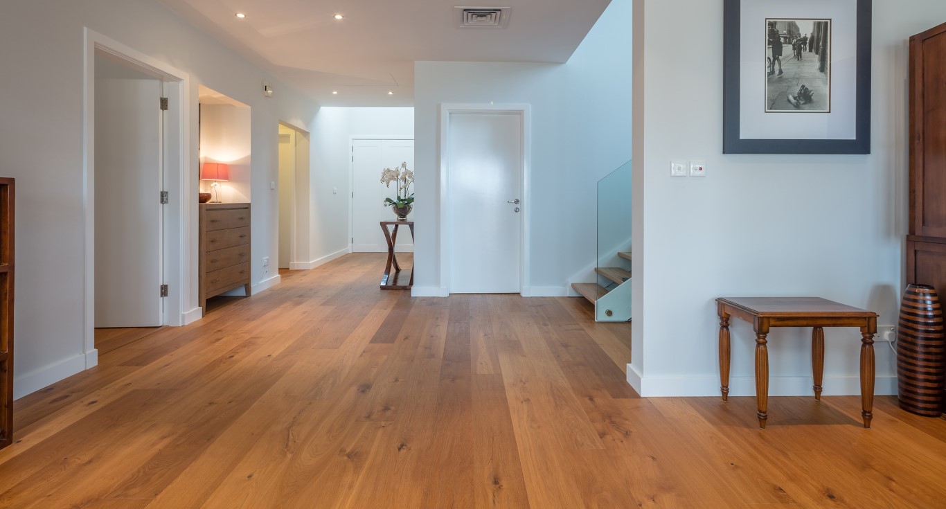 A bright home hallway in Savannah, Arabian Ranches, with warm oak flooring, white walls, and a staircase in the background.