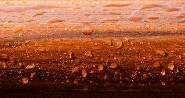 A close-up of teak wood with water droplets, highlighting its natural    water resistance and rich, golden-brown colour.