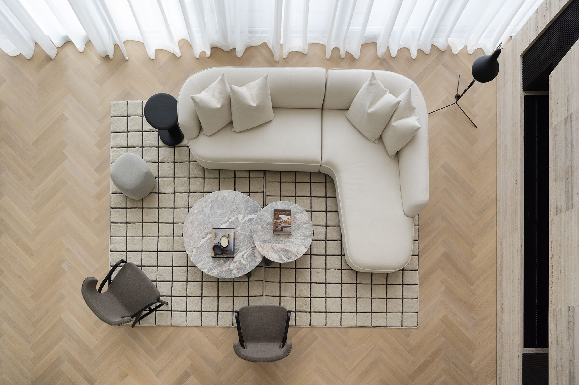 A top-down view of a modern living room with a light Herringbone wood flooring design, a cream-coloured sofa, brown chairs, and two round coffee tables.