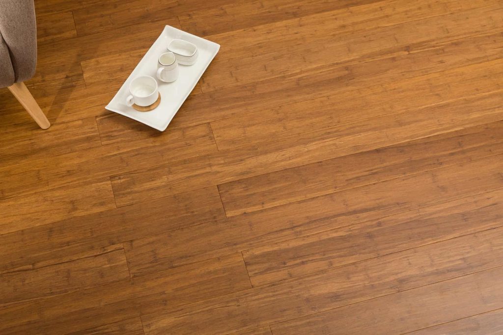 A white tray holding white cups on bamboo flooring, with a grey couch and brown feet partially visible, showcasing types of flooring.