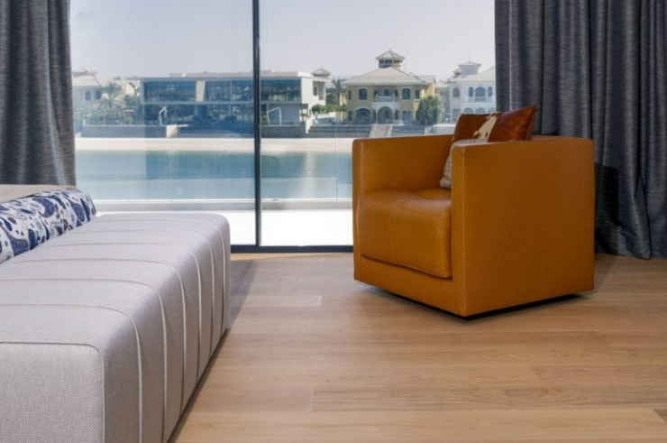 A bedroom in a Frond Villa featuring luxury vinyl flooring, an orange couch, grey bench, a blue and white mattress, and floor-to-ceiling windows with black curtains, showcasing types of flooring.