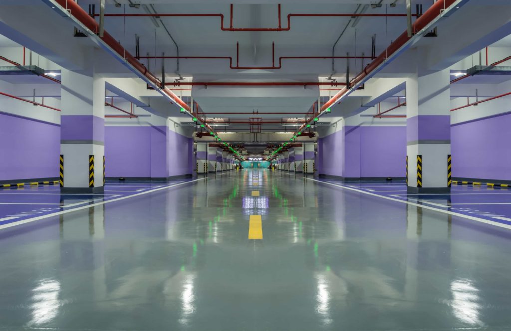 A polished epoxy floor in a parking garage with painted lane markings and overhead lighting, showcasing types of flooring.